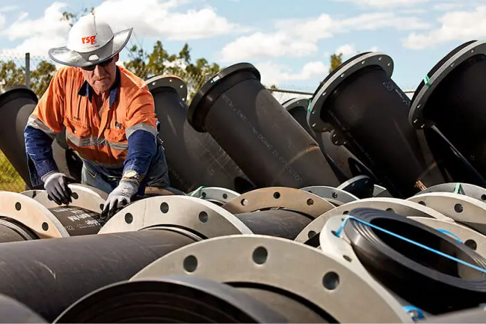 Worker inspecting and preparing large industrial pipes for assembly under a clear sky