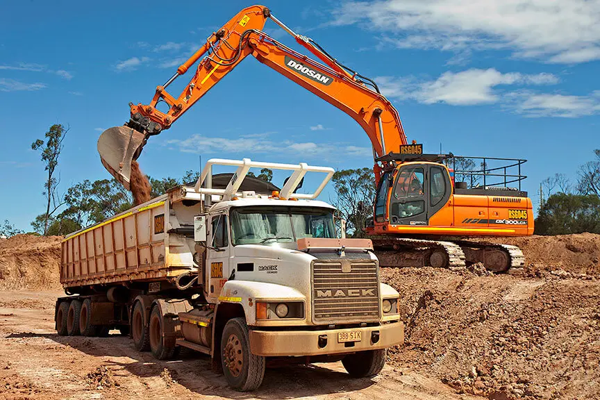 Doosan excavator loading soil into a Mack truck during a mining or construction operation