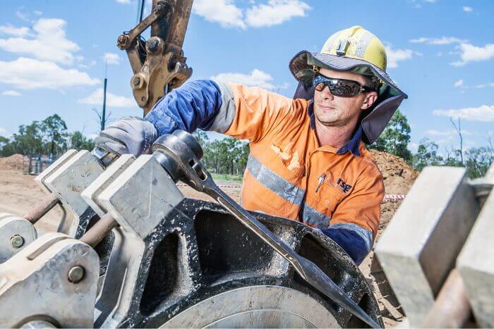 Worker in safety gear operating heavy machinery for water services under a clear blue sky