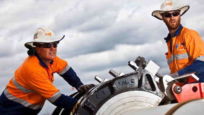 Two workers operating machinery for pipeline installation on a cloudy day